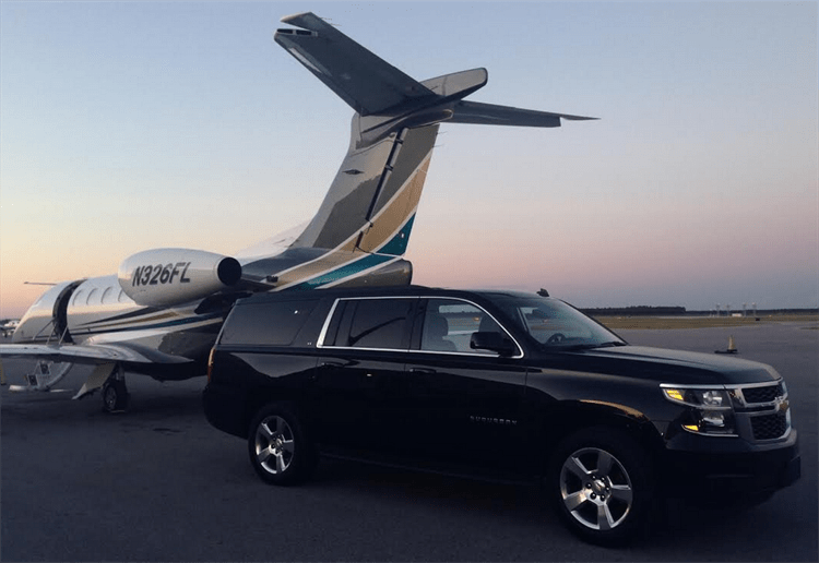Luxury SUV Airport Transfer & Wedding Chauffeured Transportation Black Chevrolet Suburban parked on the tarmac beside a private jet for luxury airport transfer and wedding transport services.