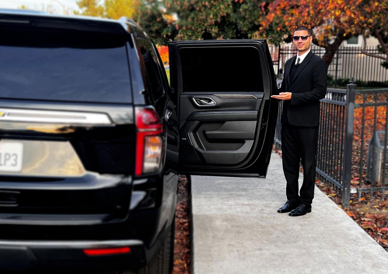 Professional chauffeur holding open the door of a black SUV.