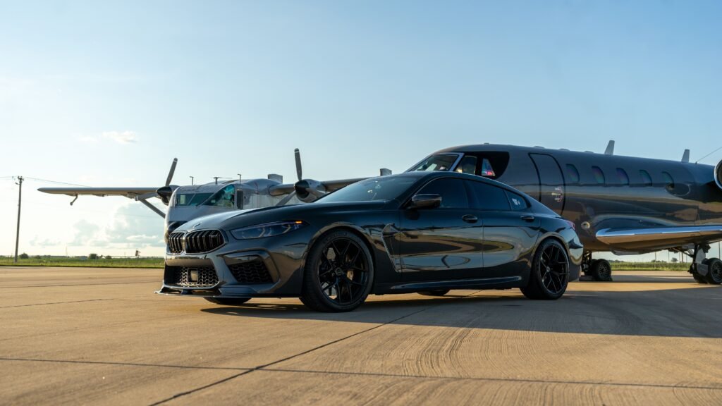 Side angle view of a sleek luxury sedan parked on the runway tarmac near a private jet at the airport.
