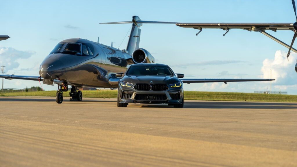 Dark metallic luxury sedan parked head-on next to a private jet on an airport tarmac for Toronto Pearson flat rate limo transfers.