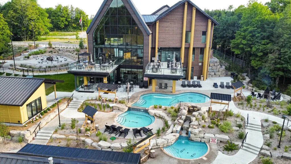 An aerial view of the Vetta Nordic Spa at Horseshoe Resort, featuring outdoor turquoise thermal pools, stone landscaping, lounging areas, and a modern timber-framed relaxation building.