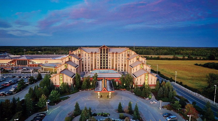 High-angle aerial view of the grand entrance of Casino Rama Resort in Orillia, Ontario, during twilight, showing the expansive hotel architecture, circular driveway, and surrounding countryside.