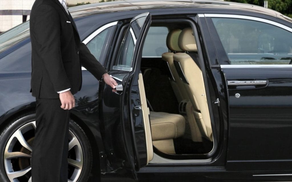 A close-up shot of a professional male chauffeur in a dark suit opening the rear door of a sleek black luxury sedan for a passenger in Orillia, Ontario.