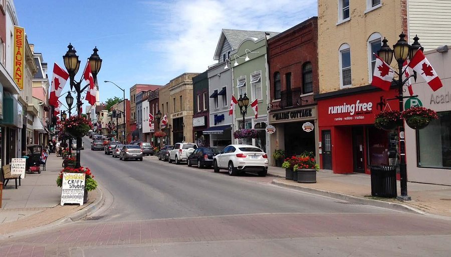 Main Street Newmarket Ontario Canada with shops, Canadian flags, parked cars, and historic downtown buildings